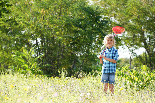 a boy holding a red net to catch moths in the overgrown garden