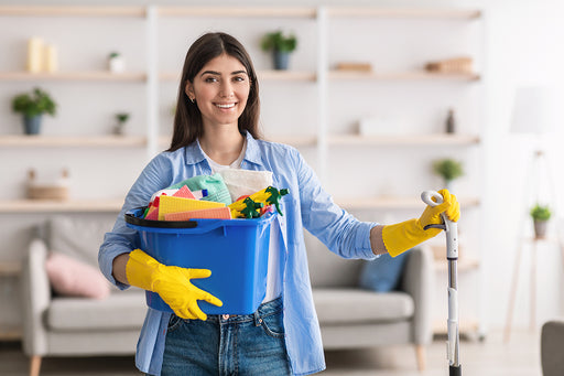 a woman at home holding a bucket of cleaning products