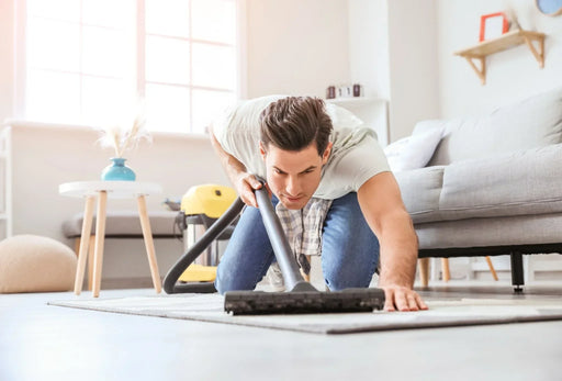 A man on his hands and knees hoovering his carpet to prevent a moth infestation