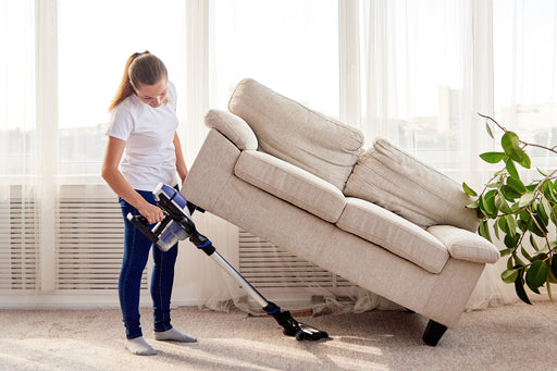 a woman lifting her couch to give her carpet a thorough vacuum