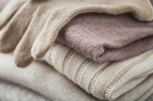 cream woolen gloves sitting on a pile of woolen sweaters