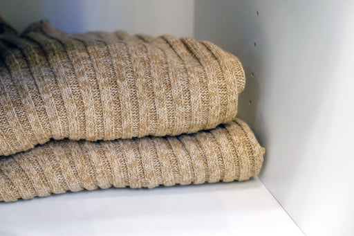folded ribbed sweaters on a shelf in a white closet