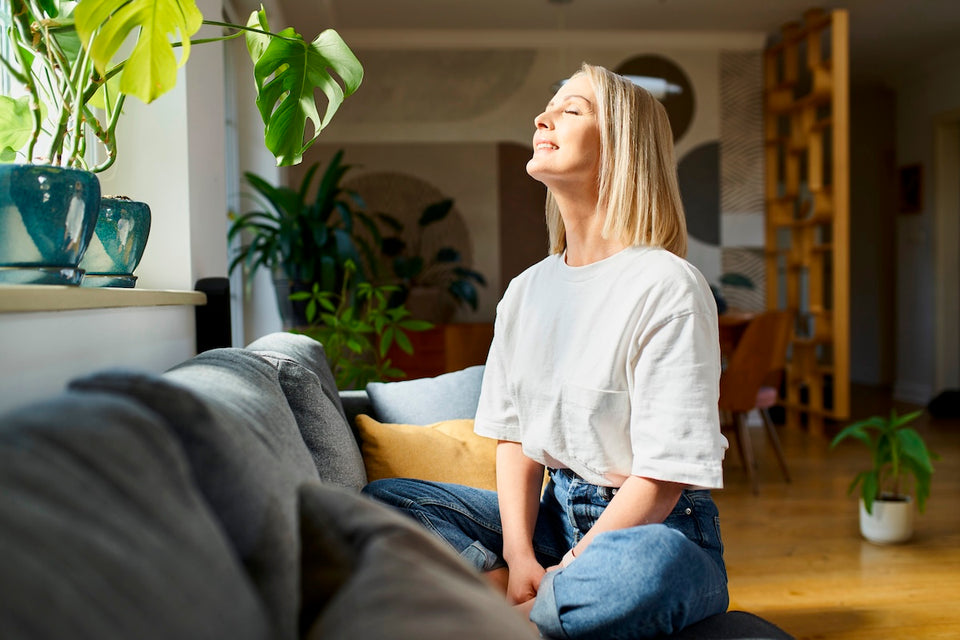 a smiling woman enjoying spring sunshine through the window in her living room