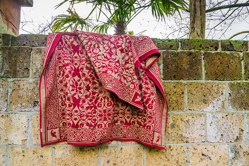 a beautiful patterned red rug placed outside on a brick wall