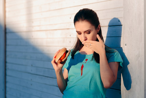 a woman holding a beef burger with tomato sauce dripped down her tee-shirt