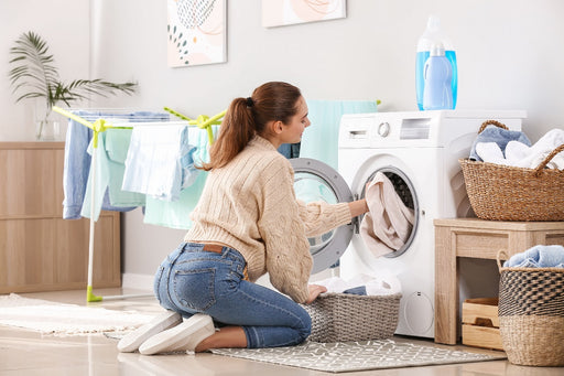 a woman kneeling by her washing machine while putting in a load of laundry