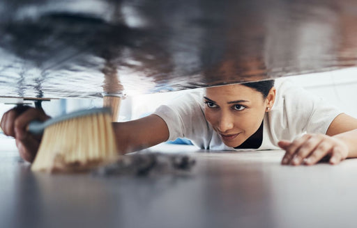 a woman thoroughly sweeping under a bed