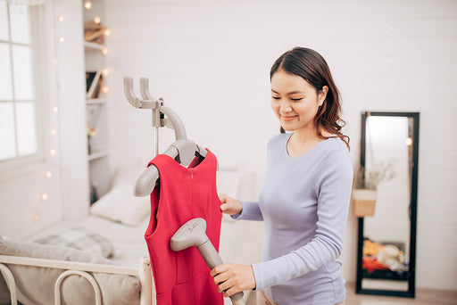 a woman using a handheld steamer to steam her red dress