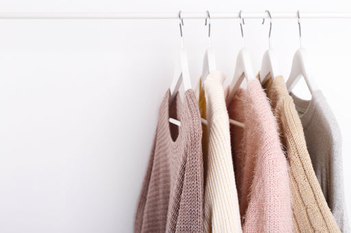 a selection of knitwear hung on white hangers on a rail