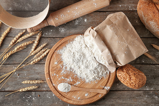 an open bag of flour on a bread board next to fresh bread and a rolling pin