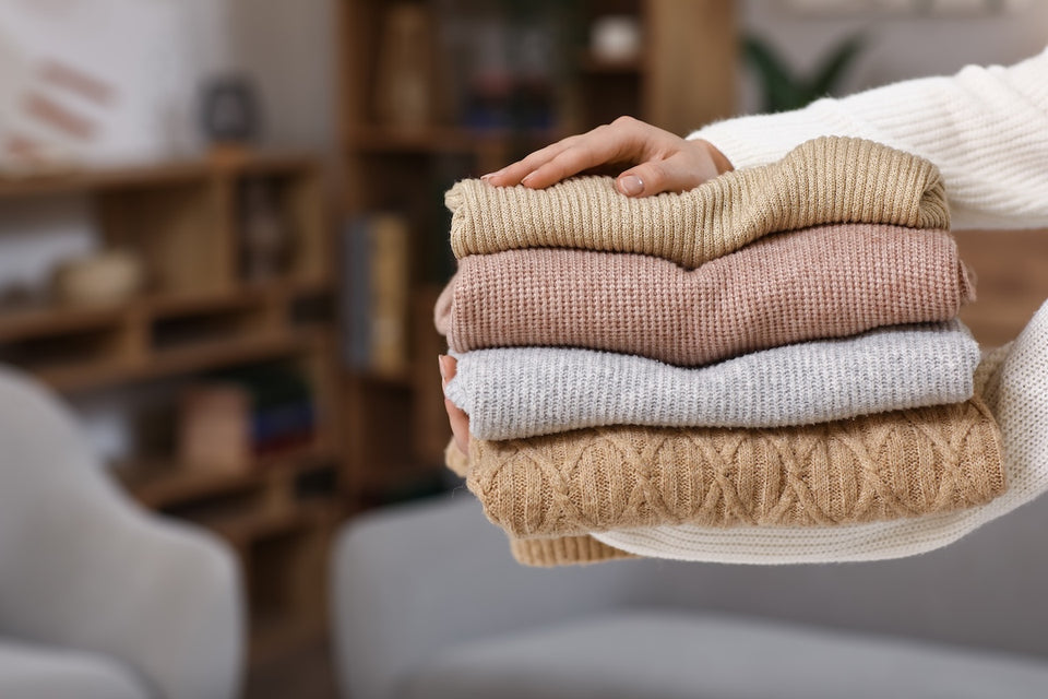 a pair of hands holding a pile of warm knitted jumpers