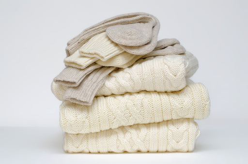 folded pile of  cream woollens with socks on the top of them