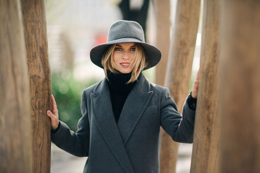 a woman standing between trees in a grey wool coat and hat