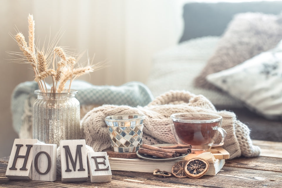 a cosy home scene with a hot drink and woollen scarf on a table with dried fruits and cinnamon sticks