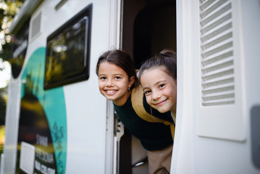 two smiling children leaning out of the door of their motorhome